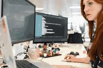 Professional exploring ai course details while coding on a laptop with dual monitors